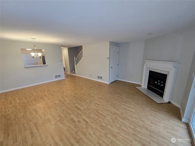 unfurnished living room featuring a tiled fireplace, light hardwood / wood-style floors, and a notable chandelier