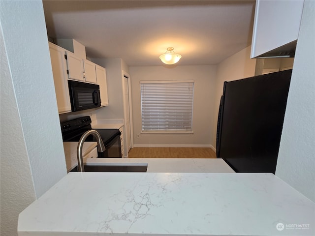 kitchen with sink, black appliances, white cabinetry, and light hardwood / wood-style flooring