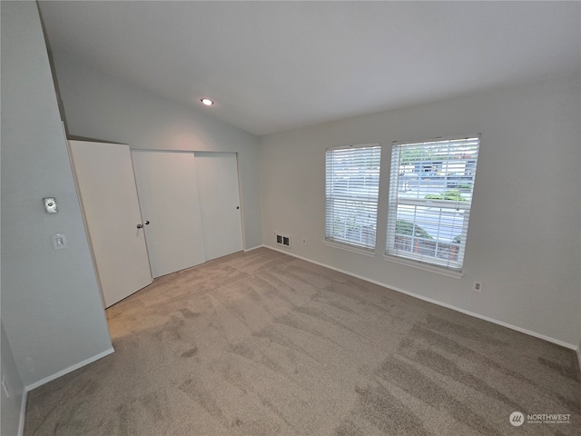 unfurnished bedroom featuring lofted ceiling, a closet, and light colored carpet