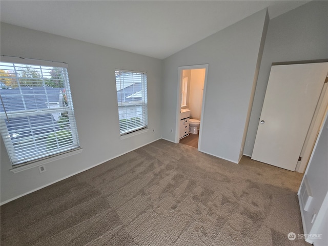 unfurnished bedroom featuring lofted ceiling, ensuite bathroom, multiple windows, and carpet