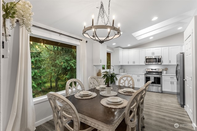 dining area featuring vaulted ceiling with skylight, an inviting chandelier, hardwood / wood-style floors, and sink