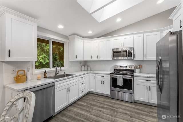 kitchen featuring white cabinets, appliances with stainless steel finishes, dark wood-type flooring, vaulted ceiling with skylight, and sink