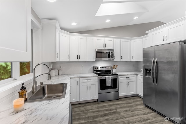 kitchen with sink, vaulted ceiling with skylight, white cabinets, appliances with stainless steel finishes, and tasteful backsplash