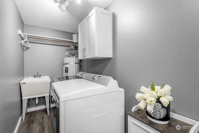 washroom with washing machine and dryer, sink, water heater, hardwood / wood-style flooring, and cabinets