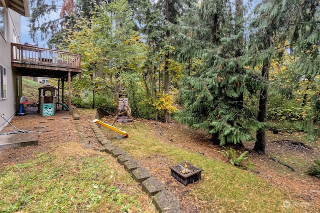 view of yard with a wooden deck, a fire pit, and a playground