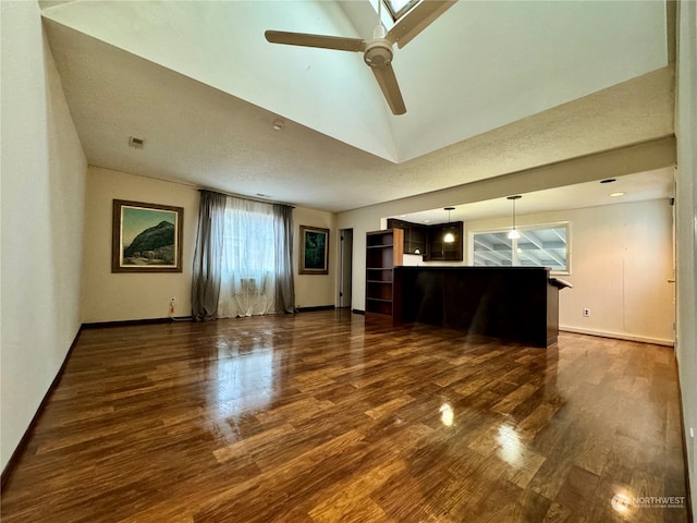 unfurnished living room featuring vaulted ceiling with skylight, dark hardwood / wood-style floors, a textured ceiling, and ceiling fan