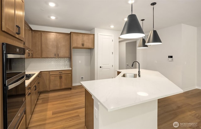 23557 Arbors Terrace Rd NE Unit 32, Kingston, WA 98346 - kitchen featuring a sink, black appliances, light wood-style floors, a center island with sink, and brown cabinets