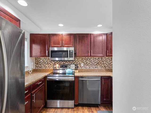 kitchen featuring light wood-type flooring, appliances with stainless steel finishes, decorative backsplash, and light stone countertops