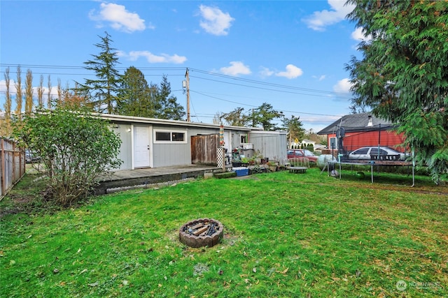 back of property with a fire pit, a trampoline, and a lawn