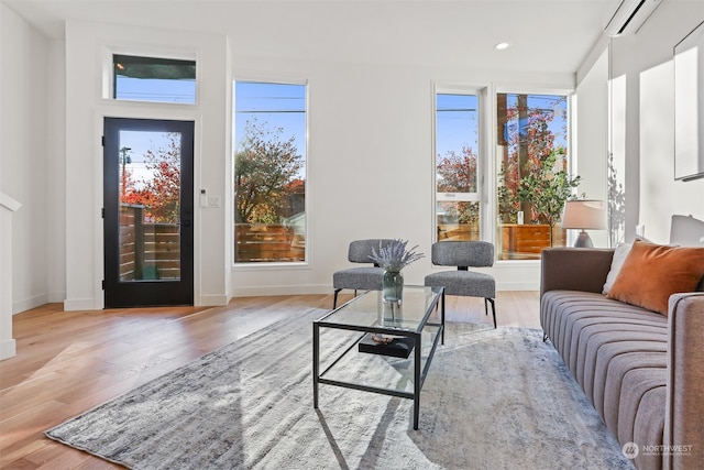 living room featuring a wall mounted air conditioner, light wood-type flooring, and a wealth of natural light