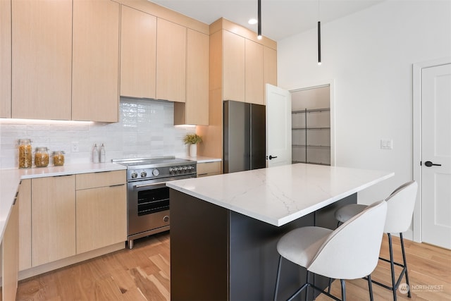 kitchen featuring light brown cabinets, light hardwood / wood-style flooring, stainless steel appliances, backsplash, and a center island