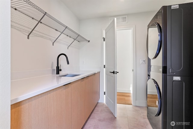 laundry room featuring stacked washer / drying machine, sink, and light tile patterned floors