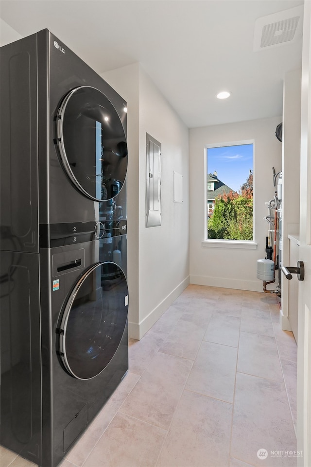 clothes washing area with stacked washing maching and dryer, electric panel, and light tile patterned floors