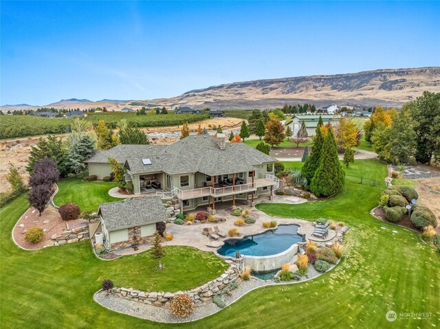 rear view of house with a fenced backyard, an outdoor pool, a deck with mountain view, a patio area, and a lawn