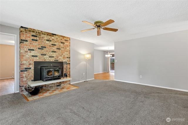 unfurnished living room featuring ceiling fan with notable chandelier, a wood stove, a textured ceiling, and carpet flooring