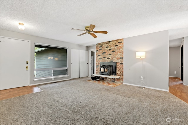 unfurnished living room featuring ceiling fan, a wood stove, a textured ceiling, and carpet