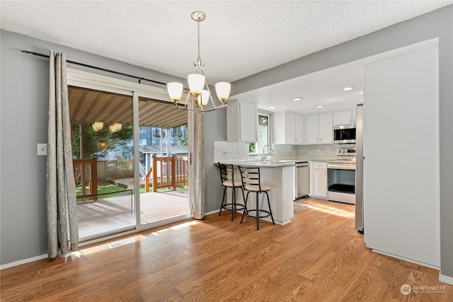 kitchen with a breakfast bar, white cabinetry, decorative light fixtures, appliances with stainless steel finishes, and light hardwood / wood-style floors