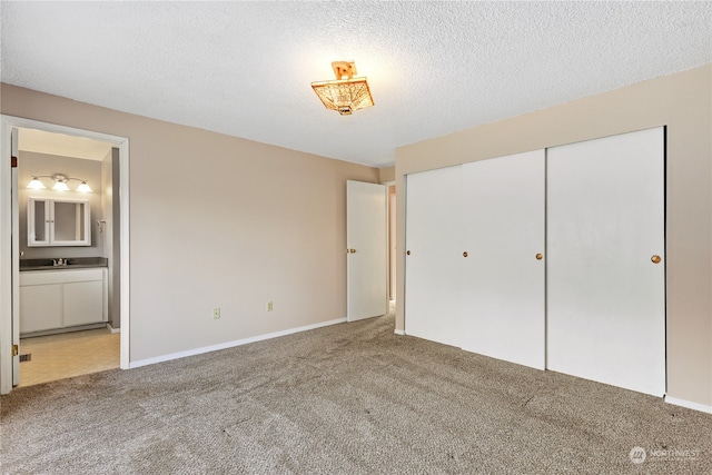 unfurnished bedroom with sink, ensuite bath, carpet, a textured ceiling, and a closet