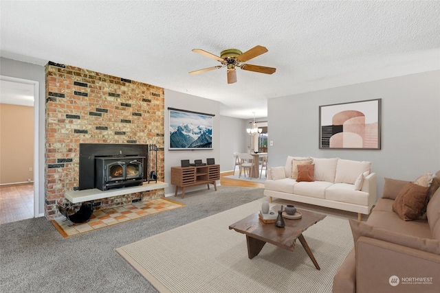 carpeted living room featuring a wood stove, ceiling fan with notable chandelier, and a textured ceiling