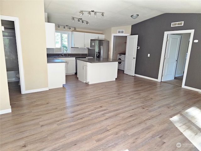 kitchen featuring washer / dryer, a kitchen island, vaulted ceiling, light hardwood / wood-style flooring, and stainless steel refrigerator with ice dispenser