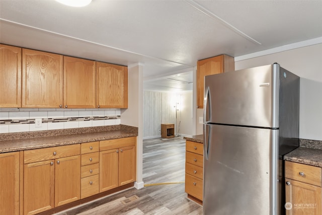 kitchen with light hardwood / wood-style floors, stainless steel fridge, light brown cabinetry, and backsplash