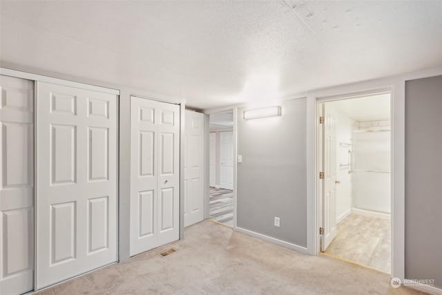 unfurnished bedroom featuring multiple closets, light carpet, and a textured ceiling