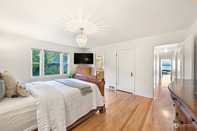 bedroom with light hardwood / wood-style floors, ensuite bath, and a chandelier