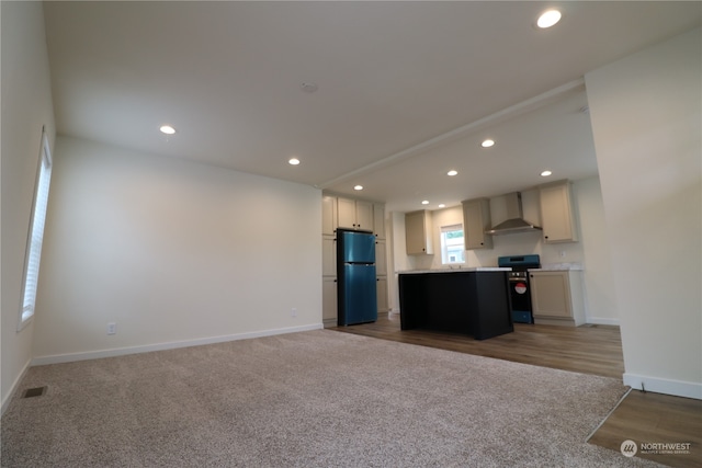 kitchen featuring wall chimney range hood, hardwood / wood-style floors, refrigerator, a center island, and electric range oven