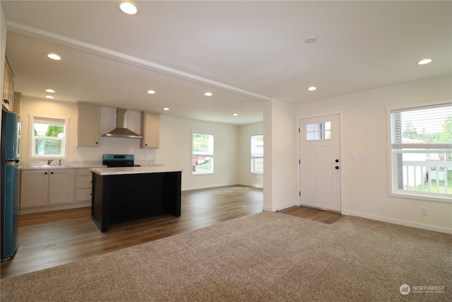 kitchen with wall chimney range hood, plenty of natural light, a kitchen island, and stainless steel stove