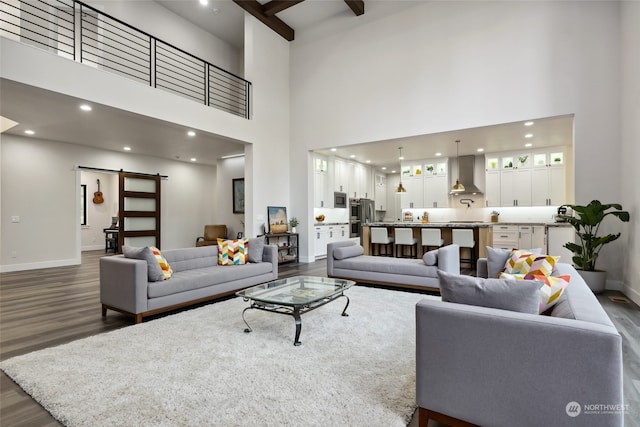 living room featuring beam ceiling, a high ceiling, a barn door, and dark hardwood / wood-style flooring