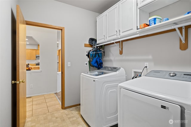 laundry room with light tile patterned flooring, washing machine and clothes dryer, and cabinets