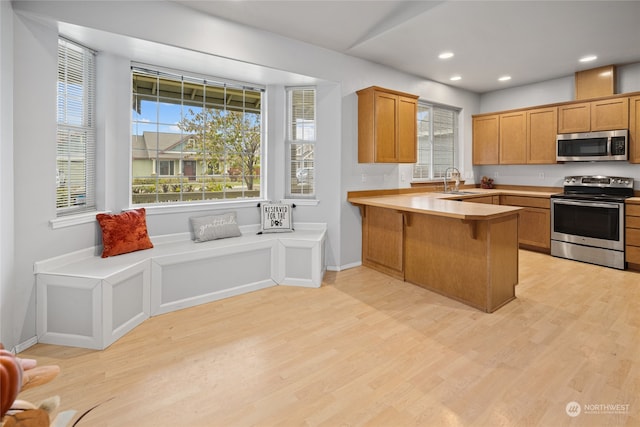 kitchen with sink, kitchen peninsula, a breakfast bar area, stainless steel appliances, and light hardwood / wood-style flooring