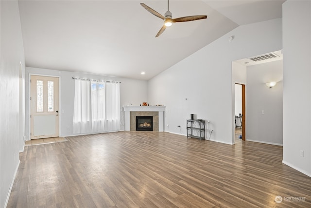 unfurnished living room featuring lofted ceiling, ceiling fan, a tiled fireplace, and dark hardwood / wood-style flooring