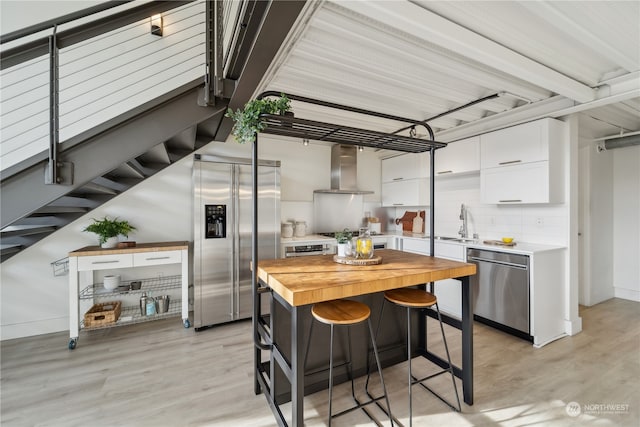 kitchen with white cabinetry, stainless steel appliances, wall chimney range hood, and light hardwood / wood-style flooring