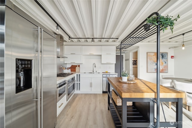 kitchen with light hardwood / wood-style floors, sink, appliances with stainless steel finishes, white cabinets, and wall chimney range hood