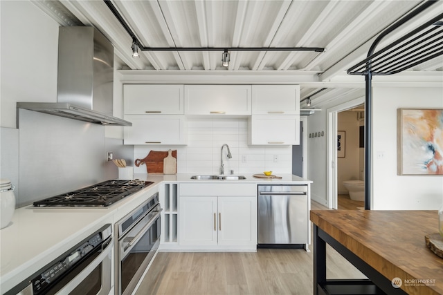 kitchen with white cabinets, appliances with stainless steel finishes, sink, and wall chimney range hood