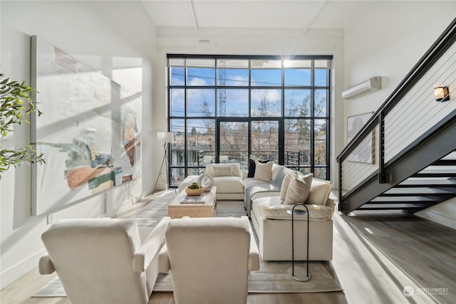 living room with a towering ceiling, a wealth of natural light, light hardwood / wood-style floors, and an AC wall unit