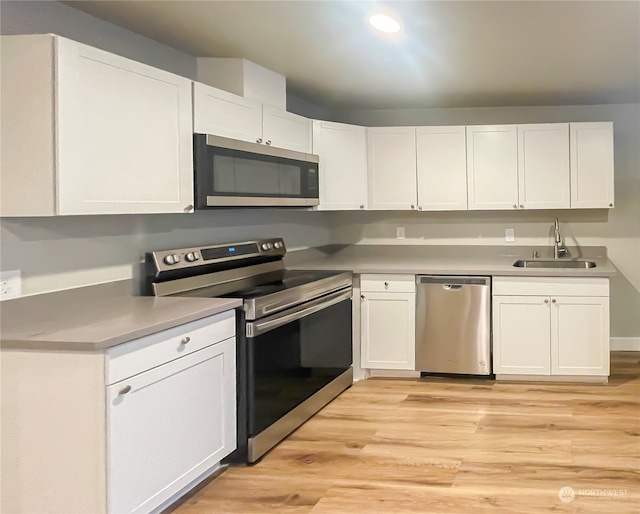 kitchen with stainless steel appliances, white cabinetry, and light hardwood / wood-style flooring