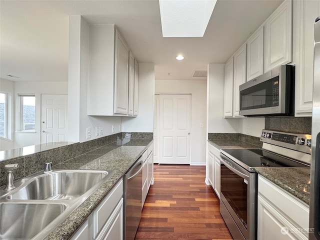 kitchen with stainless steel appliances, dark hardwood / wood-style flooring, white cabinets, sink, and a skylight