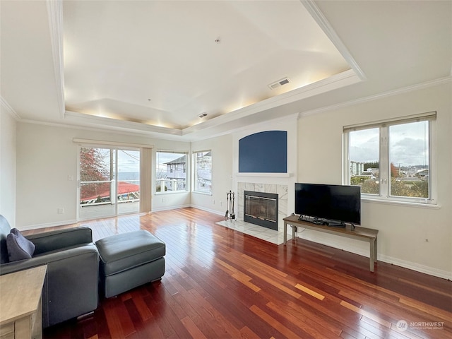 living room with hardwood / wood-style flooring, ornamental molding, a premium fireplace, and a tray ceiling