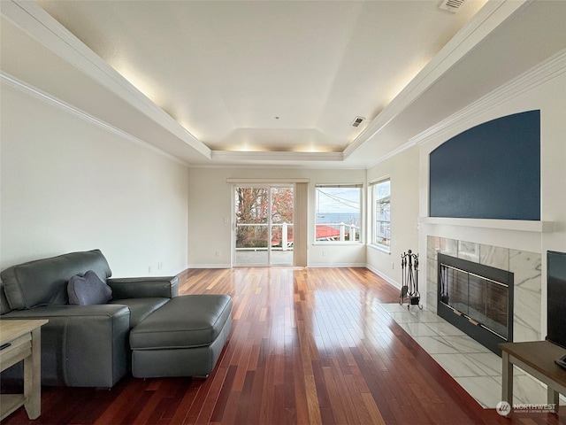 living area with crown molding, wood-type flooring, a raised ceiling, and a tile fireplace