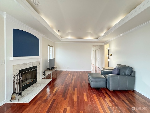 living area with hardwood / wood-style floors, a raised ceiling, ornamental molding, and a fireplace