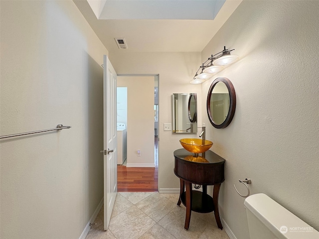 bathroom with toilet, sink, tile patterned flooring, and washer / dryer