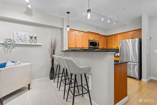 kitchen featuring light wood-type flooring, kitchen peninsula, stainless steel appliances, decorative light fixtures, and track lighting