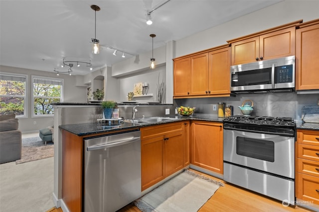 kitchen with dark stone countertops, stainless steel appliances, decorative light fixtures, and sink