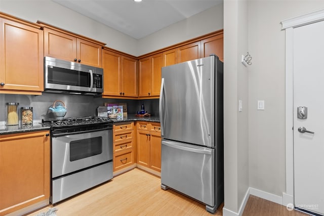 kitchen with decorative backsplash, appliances with stainless steel finishes, light hardwood / wood-style floors, and dark stone countertops