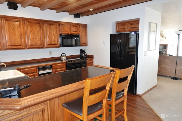 1399 Ocean Shores Blvd SW Unit 2N-E, Ocean Shores, WA 98569 - kitchen featuring black appliances, brown cabinets, dark countertops, a kitchen breakfast bar, and a wooden ceiling with exposed beams