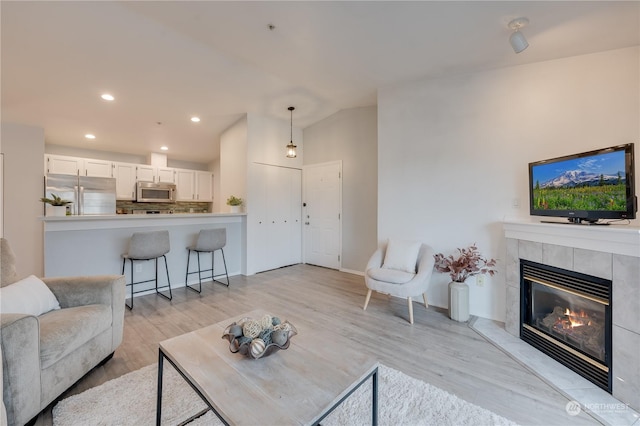 living room with lofted ceiling, a tile fireplace, and light wood-type flooring