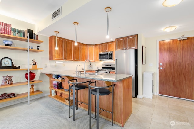 kitchen with appliances with stainless steel finishes, sink, kitchen peninsula, pendant lighting, and light stone counters