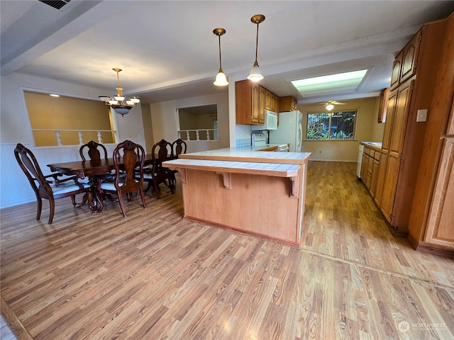 kitchen with white appliances, light wood-type flooring, kitchen peninsula, hanging light fixtures, and a breakfast bar